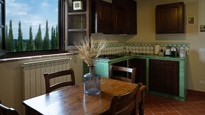Una cocina con armarios de madera, salpicadero de azulejos verdes y ventana con vistas a árboles.