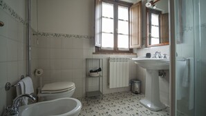 Un baño con inodoro, bidé, lavabo y una ventana con contraventanas de madera.