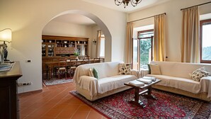 A living room with two sofas, a coffee table, and a patterned rug. There is a dining area with wooden furniture and a kitchen visible through an archway. - Nice apartment for 10 people with A/C, WIFI, pool and panoramic view, close to San Gimignano (Montauto)