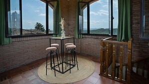 A room with large windows, a brick wall, a round table with stools, and a wooden staircase. - Nice apartment for 10 people with A/C, WIFI, pool and panoramic view, close to San Gimignano (Montauto)