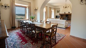 A dining area with a wooden table and chairs, a red patterned rug, and a view of a bedroom with a fireplace. - Nice apartment for 10 people with A/C, WIFI, pool and panoramic view, close to San Gimignano (Montauto)