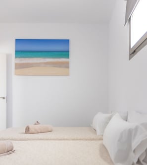 Ein Schlafzimmer mit einem Bett, einem zusammengerollten Handtuch und einem Bild eines Strandes.