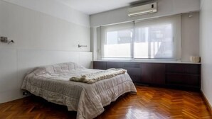 A bedroom with a bed, wooden flooring, a window with blinds, and an air conditioning unit. - SEMIPISO PALERMO  (Buenos Aires)