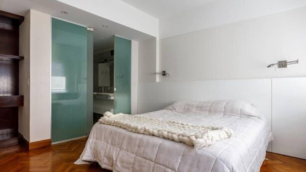 A bedroom with a bed, a wooden wardrobe, and a glass door leading to a bathroom. - SEMIPISO PALERMO  (Buenos Aires)