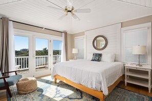 A bedroom with a large bed, a ceiling fan, a view through the sliding glass doors, and a small seating area. - Here & Now: Semi-Oceanfront, private pool, hot tub, steps to the beach, two living areas. (Southern Shores)