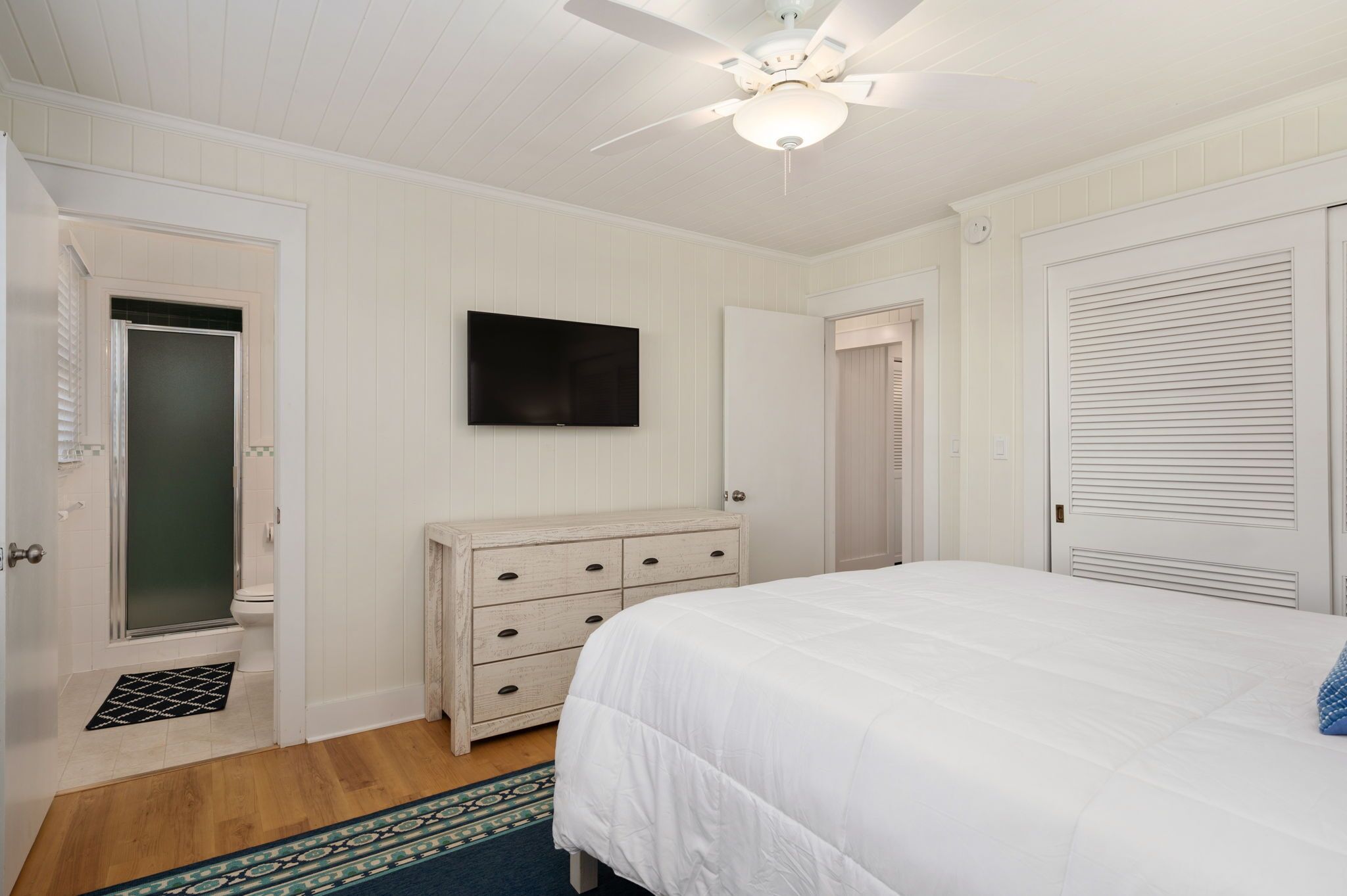 A bedroom with a bed, a dresser, a ceiling fan, and a TV.