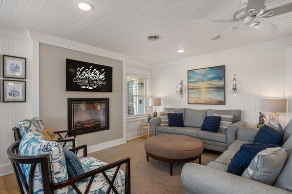 A living room with a fireplace, a sofa set, a coffee table, and artwork on the walls. - Here & Now: Semi-Oceanfront, private pool, hot tub, steps to the beach, two living areas. (Southern Shores)