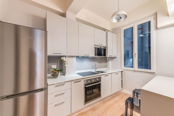 A modern kitchen with stainless steel appliances, white cabinetry, and a window with blue-tinted glass.
