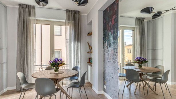 Un coin repas avec une table ronde, des chaises grises et un vase de fleurs.