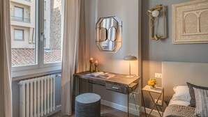 Une chambre moderne avec un bureau, une lampe, une petite table d’appoint ornée de fleurs, un radiateur et une fenêtre avec des rideaux.