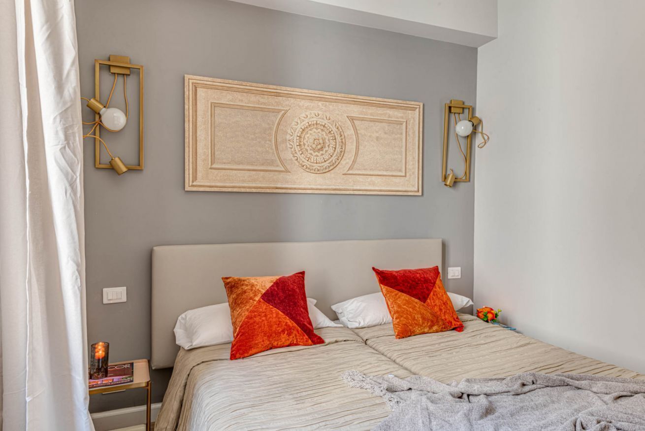 A bedroom with a bed, pillows, a wall-mounted light fixture, and a decorative panel.