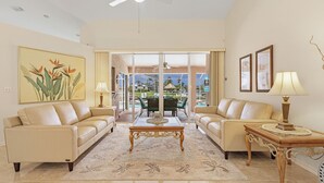 A spacious living room with a large window, two sofas, a coffee table, and a ceiling fan. - Bikes, Kayaks, Amazing Water views, Gulf Access & Heated Pool - Edgewater Oasis- Roelens Vacations (Cape Coral)