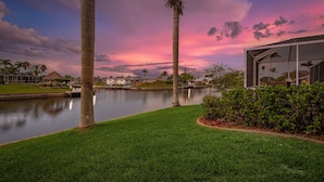 A waterfront property with a modern house, a grassy area, and a calm lake. - Bikes, Kayaks, Amazing Water views, Gulf Access & Heated Pool - Edgewater Oasis- Roelens Vacations (Cape Coral)
