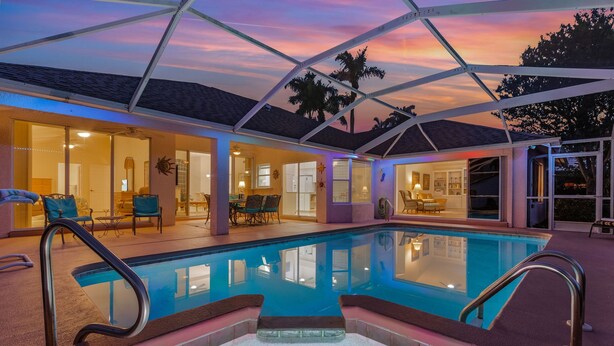 A swimming pool with a glass enclosure, surrounded by a covered patio area with seating and a view of the interior. - Bikes, Kayaks, Amazing Water views, Gulf Access & Heated Pool - Edgewater Oasis- Roelens Vacations (Cape Coral)