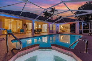 Piscina com estrutura de vidro, cercada por um alpendre coberto com assentos e vista para o interior.