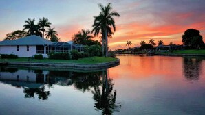 A house with a covered patio and a calm water body reflecting the structure. - Bikes, Kayaks, Amazing Water views, Gulf Access & Heated Pool - Edgewater Oasis- Roelens Vacations (Cape Coral)