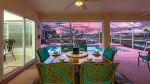 A dining area with a pool view, outdoor seating, and a ceiling fan. - Bikes, Kayaks, Amazing Water views, Gulf Access & Heated Pool - Edgewater Oasis- Roelens Vacations (Cape Coral)