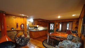 A cozy cabin interior with a wooden dining area, a kitchen with wooden cabinets, and a fireplace.