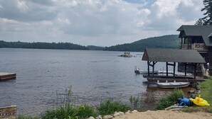 A lakeside view with a wooden dock, a covered pavilion, and a sign warning of a rip current.