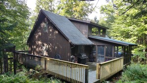 A wooden cabin with a covered porch, surrounded by dense forest.