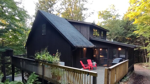 A cabin with a deck, two red chairs, and a small table.