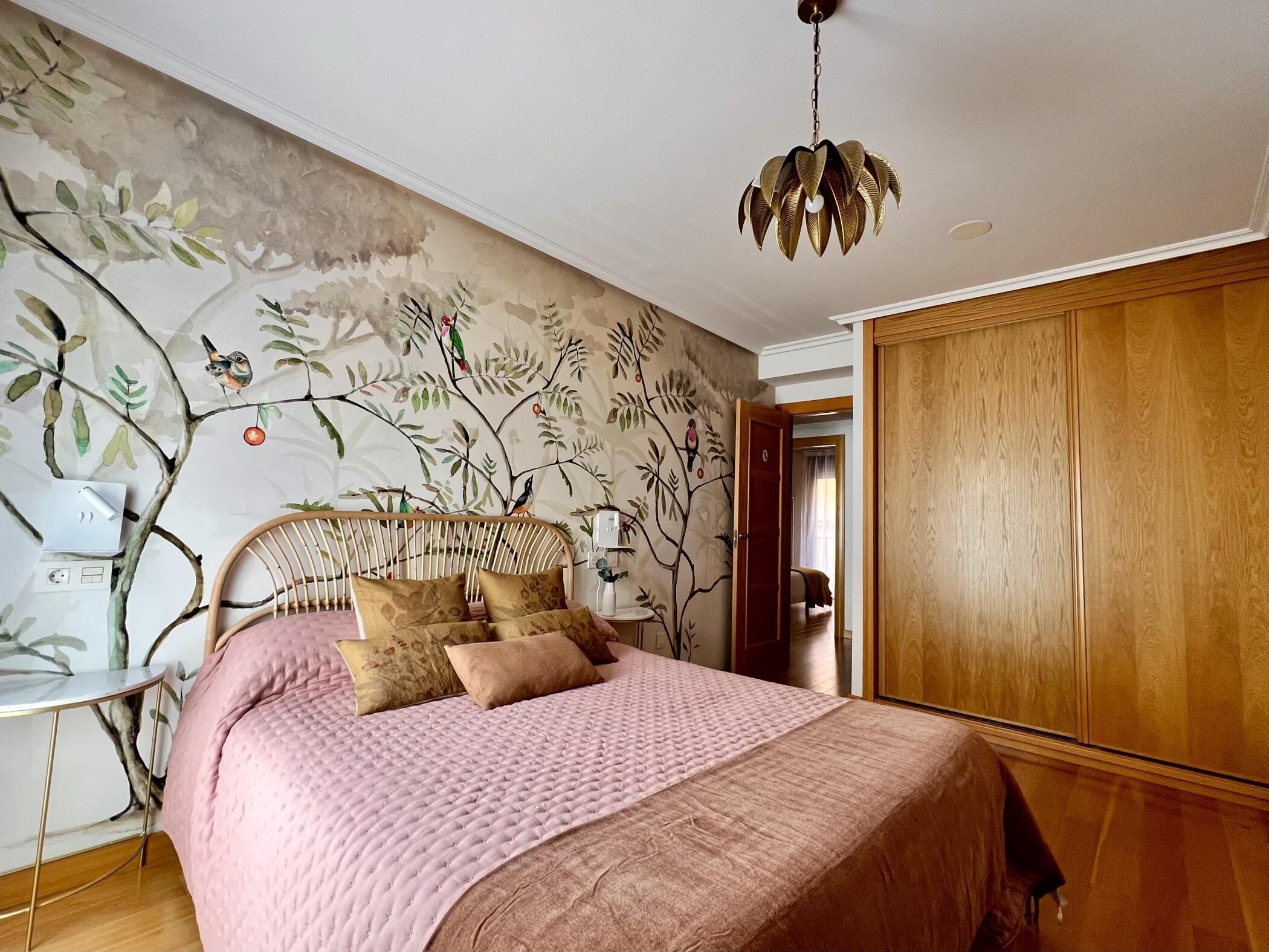 A bedroom with a bed, a wooden wardrobe, a wall with a nature-themed mural, and a hanging light fixture.