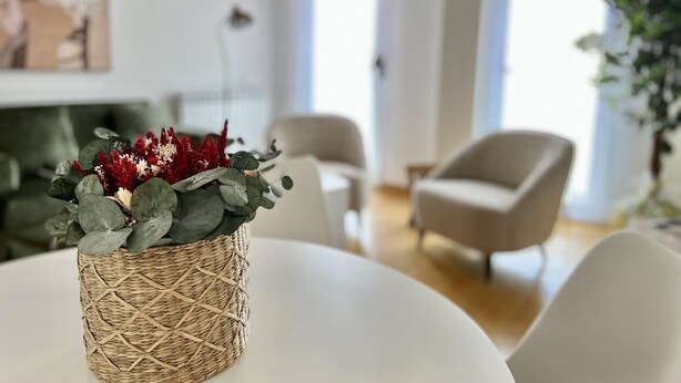 Un saló modern amb una taula rodona, una cistella de vimet amb flors i un sofà.