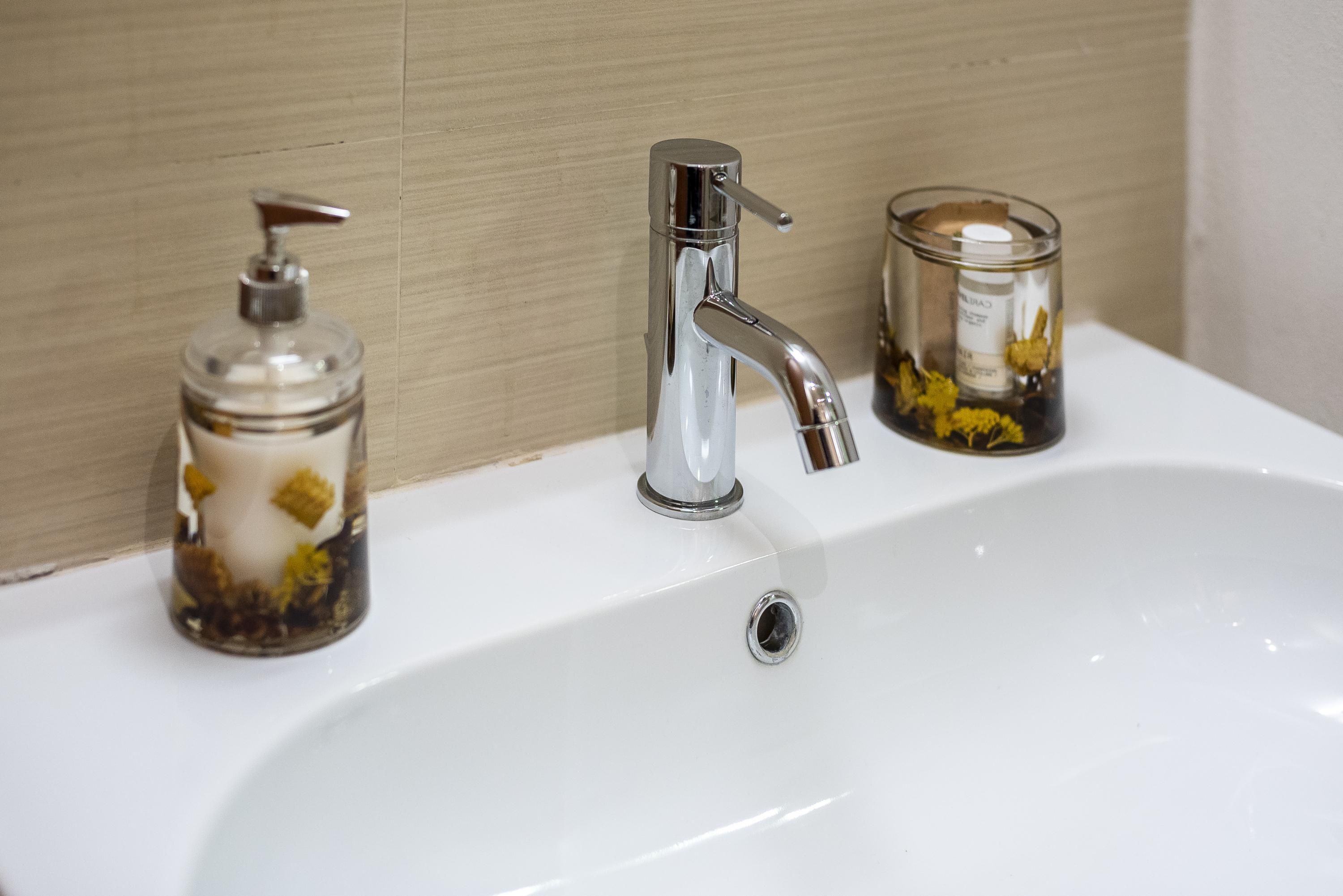 Un lavabo de salle de bain avec un robinet chromé, un distributeur de savon et une bougie.