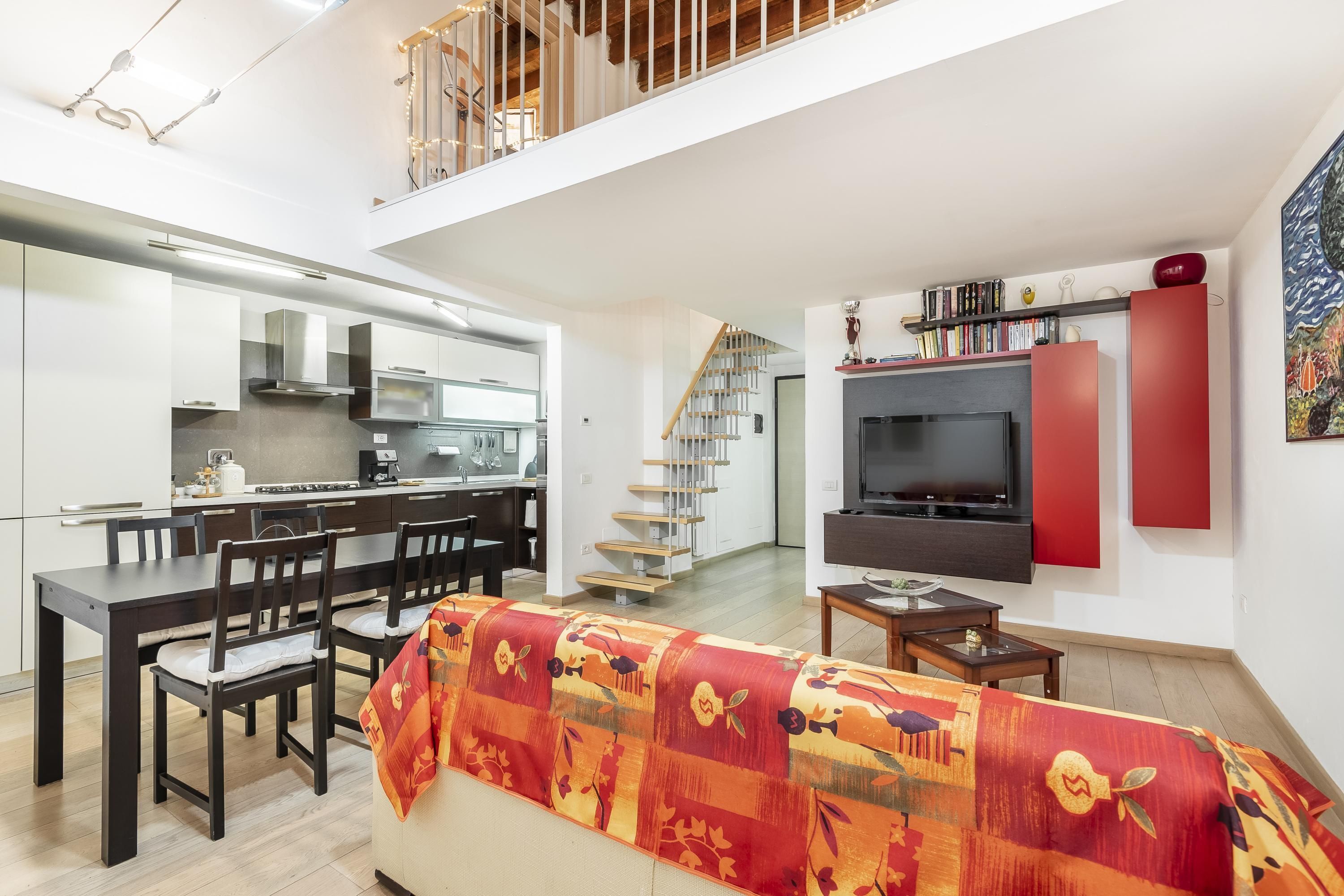 A modern apartment with a dining area, kitchen, staircase, living room, and TV.