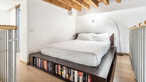 Un dormitorio con una cama, una estantería, un radiador y techo de madera.