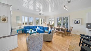 A spacious living room with a blue sectional sofa, a coffee table, and patterned chairs. There is a dining area with a wooden table and chairs. - Surfer Dog 4 Bedroom Home by RedAwning (Panama City Beach)