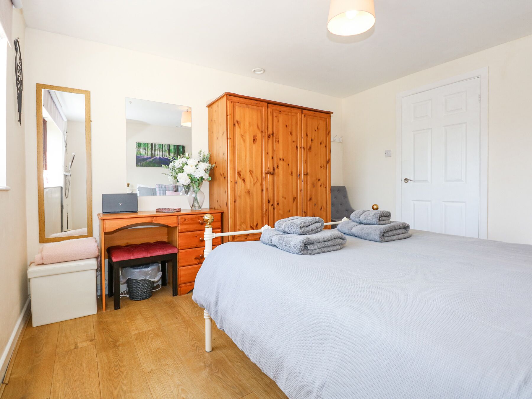 A bedroom with a bed, wooden wardrobe, desk, and a mirror.