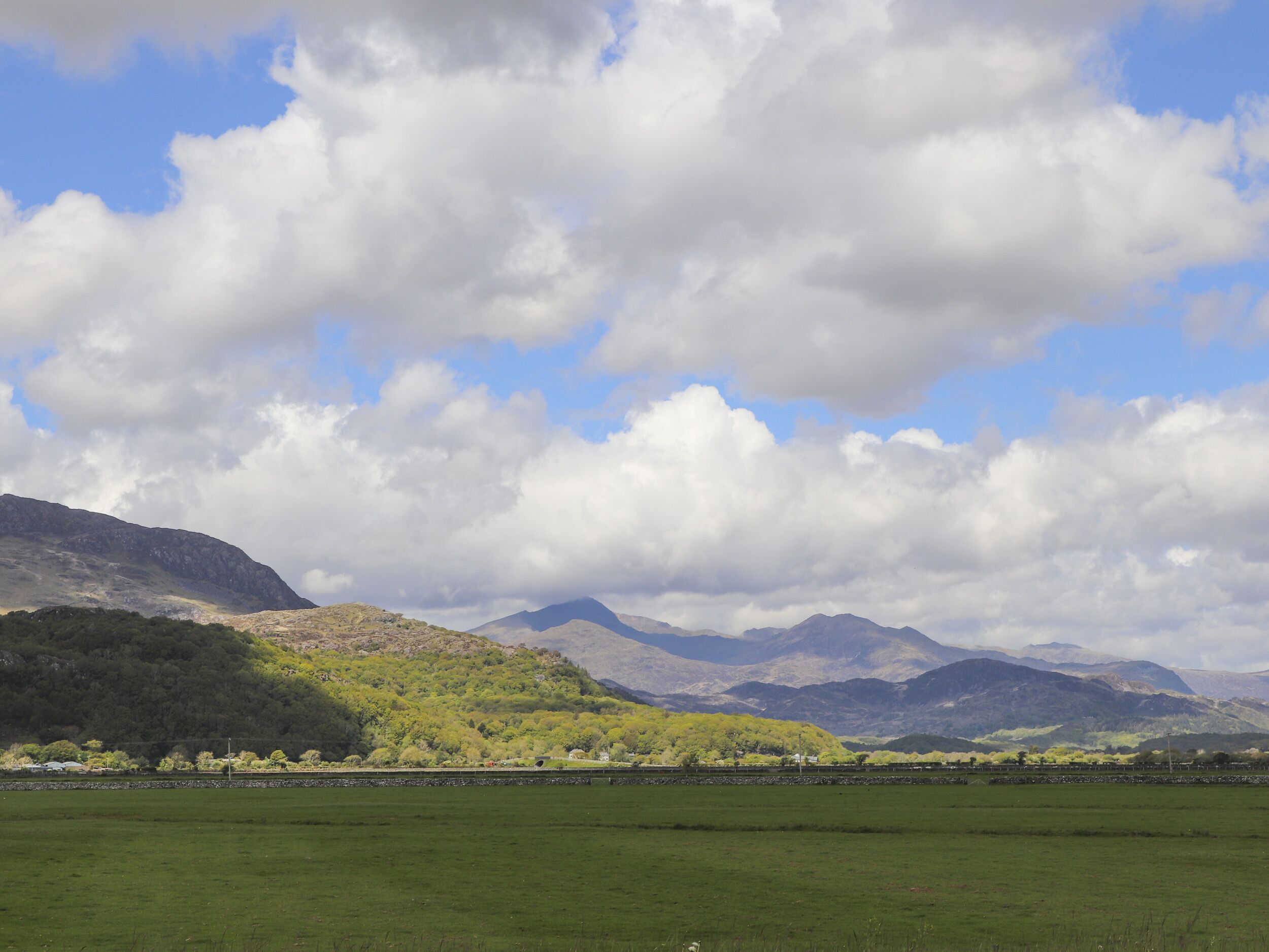 Un paisaje con colinas ondulantes, cielo despejado y una cordillera distante.