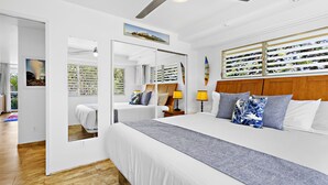 A modern bedroom with a large bed, a wooden headboard, and a view of a garden through a sliding door.