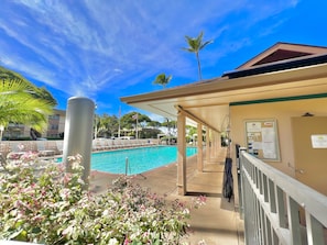 A pool area with lounge chairs, a covered seating area, and a bulletin board with notices.