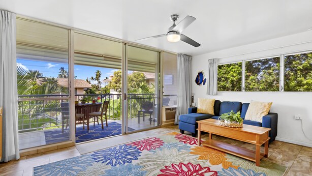 A spacious living room with a blue sofa, a wooden coffee table, and a colorful floral rug.