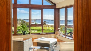 Ein Zimmer mit großen Fenstern, Korbmöbeln und Blick auf einen See und Grünflächen.
