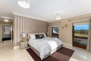 Une chambre moderne avec un grand lit, des lampes de chevet, une vue à travers une porte coulissante et une petite table de chevet.