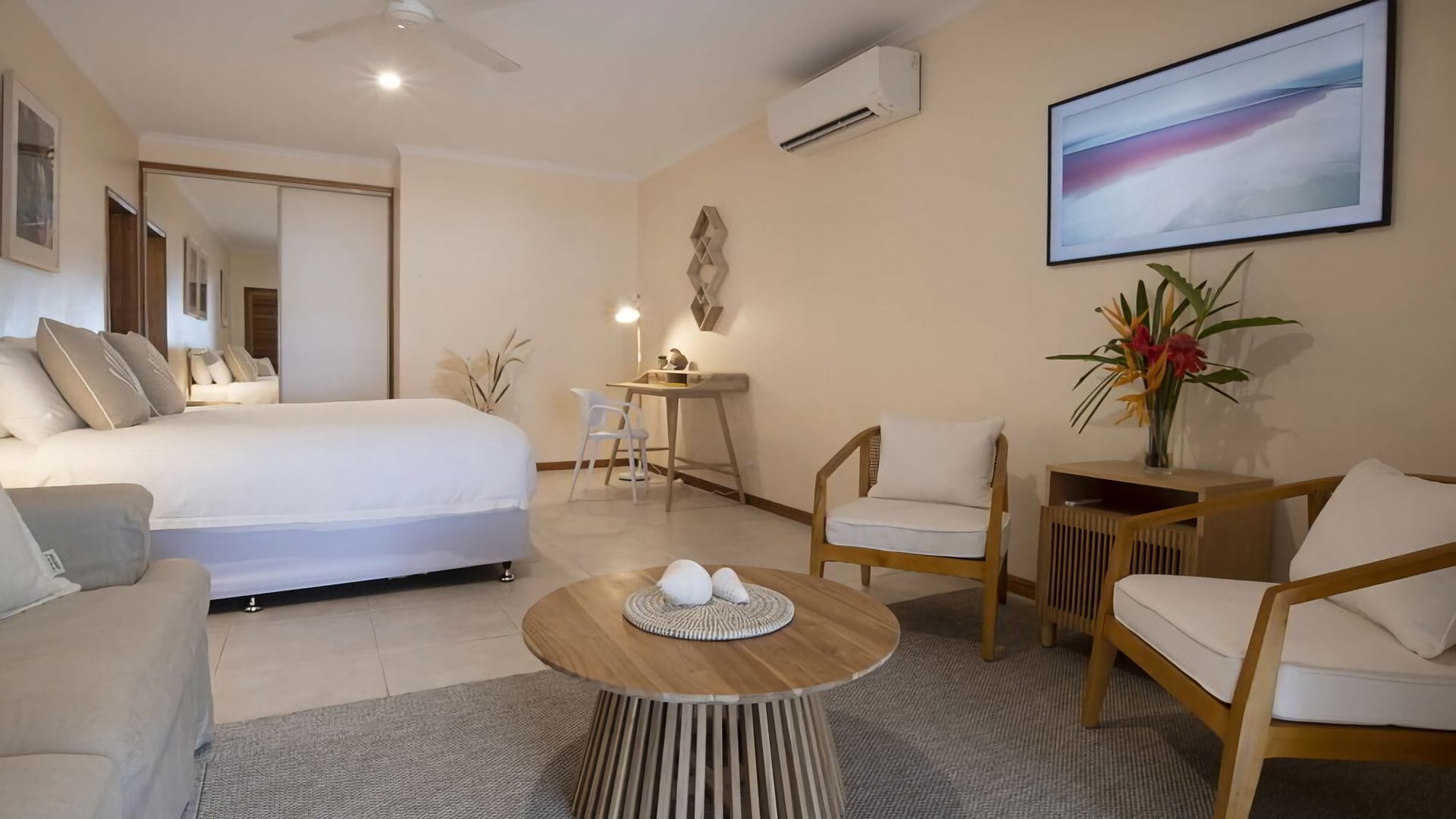 A hotel room with a bed, two chairs, a small round table, and a desk with a chair.