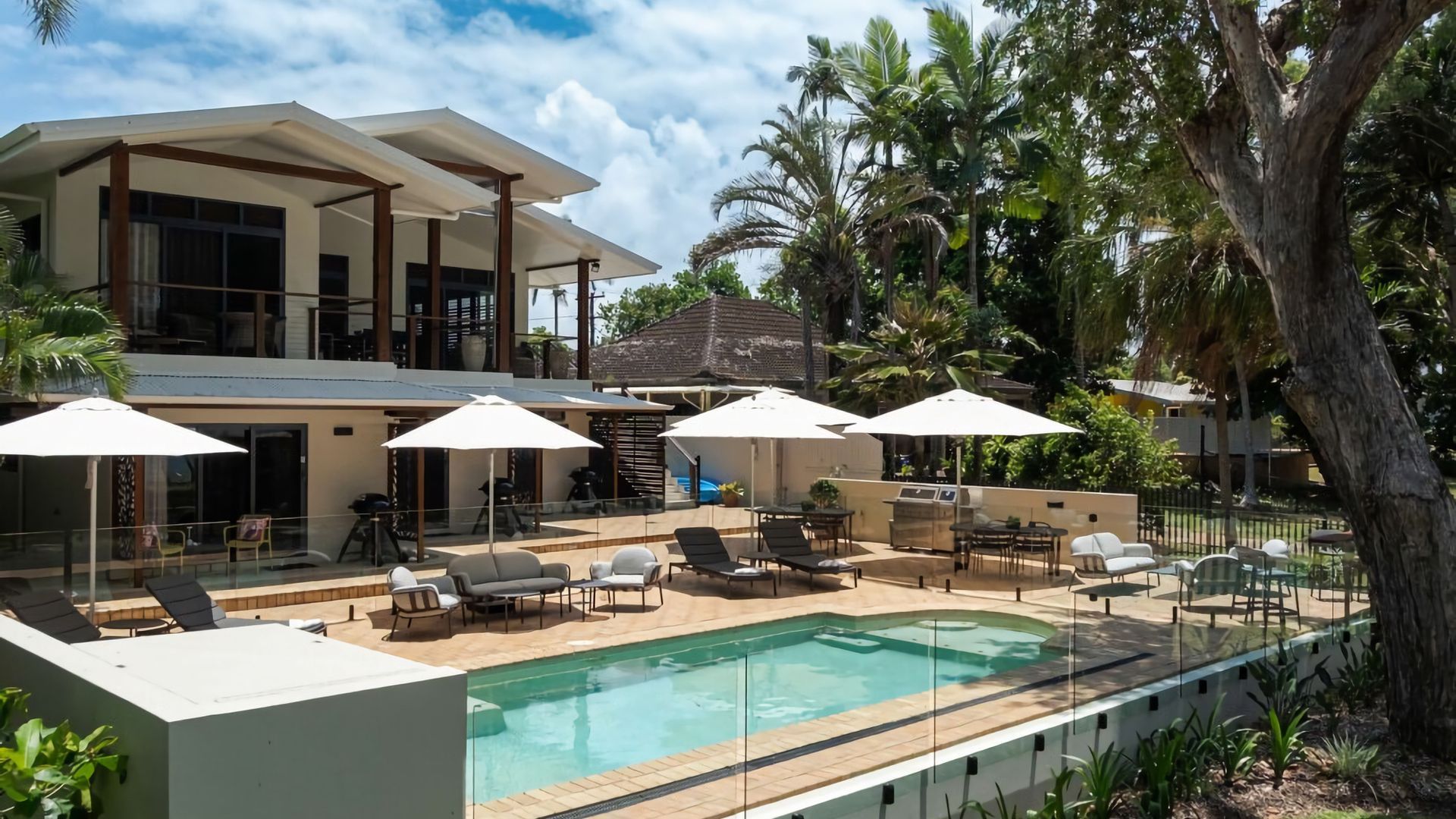Ein moderner Poolbereich mit Liegestühlen und Sonnenschirmen, umgeben von üppigem Grün und einem großzügigen Haus.