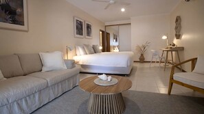 A modern bedroom with a bed, a sofa, a round wooden coffee table, and a dining area with a chair and table.