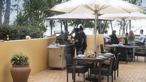 An outdoor dining area with tables, chairs, and umbrellas, overlooking a body of water.