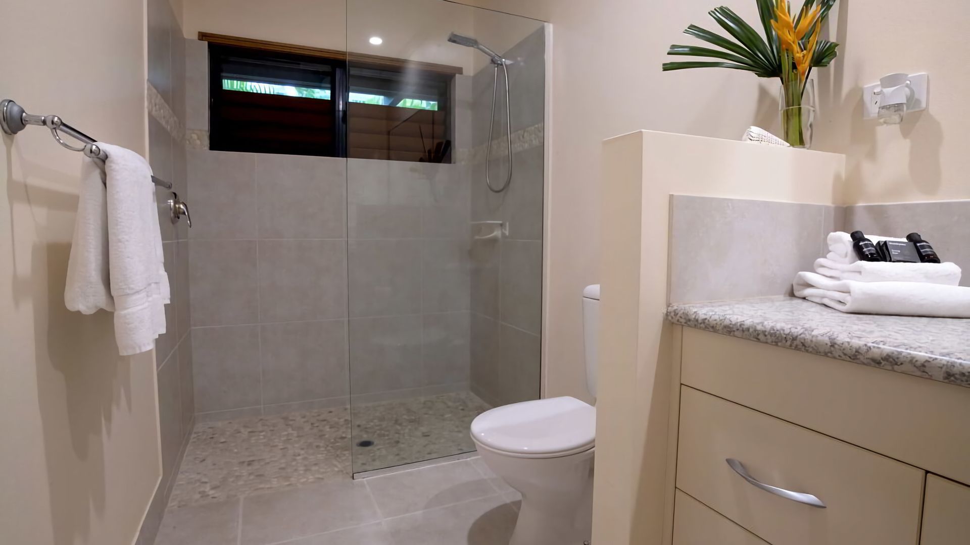 Une salle de bain moderne avec une douche à parois de verre, des toilettes et un meuble-lavabo agrémenté de serviettes et d’articles de toilette.