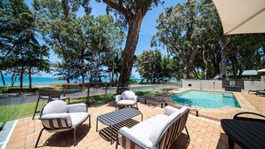 Un'area affacciata sulla piscina con mobili da esterno, vista sull'oceano e un albero grande.