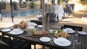 An outdoor dining area with a pool in the background, equipped with tables, chairs, and various dining items.