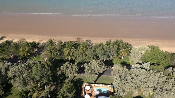 An aerial view of a beachside property with a swimming pool and lush vegetation.