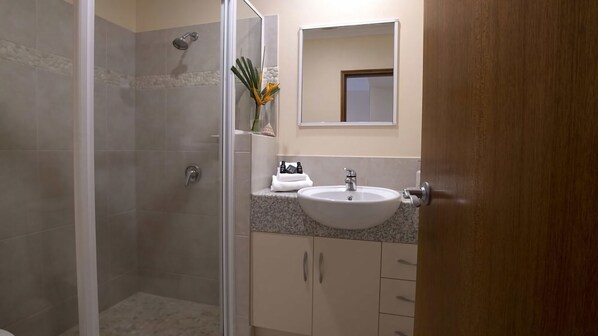 A bathroom with a shower, sink, and cabinets.