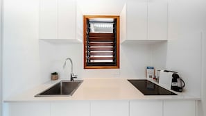 A modern kitchen with a built-in oven, a sink, and a window with blinds.