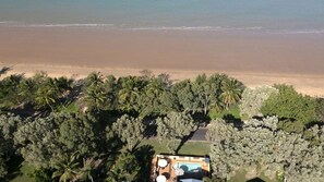 Eine Vogelperspektive zeigt ein Anwesen am Strand mit Schwimmbad und üppiger Vegetation.