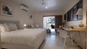 A hotel room with a bed, a desk, and a chair. There is a window and a door leading to an outdoor area.